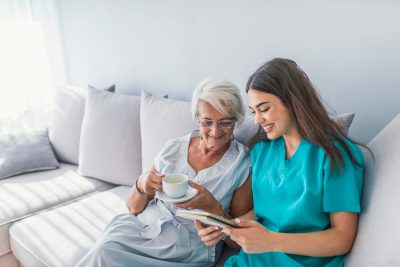 caregiver is reading the book and senior woman is listeing while having a coffee